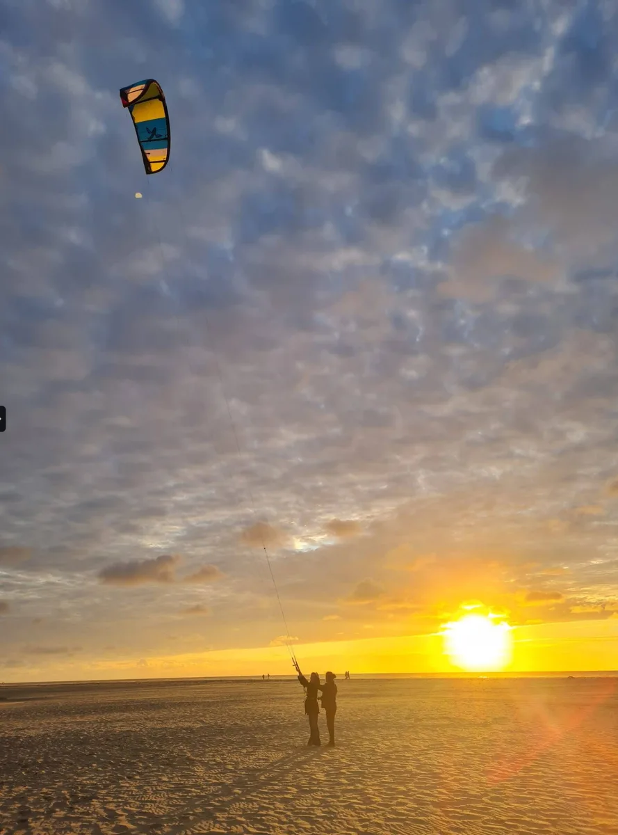 Grupo en la playa al atardecer con cometa de kitesurf